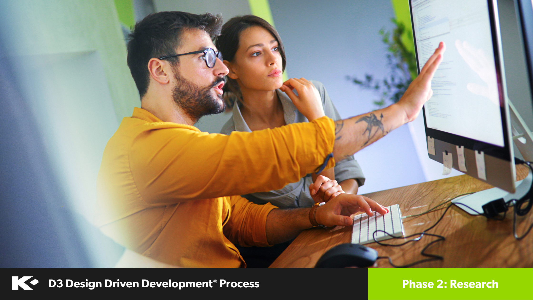 Two people sit at a desk, focused on a computer screen. One points at the monitor while the other watches closely. The image includes a banner labeled "D3 Design Driven Development Process, Phase 2: Research.