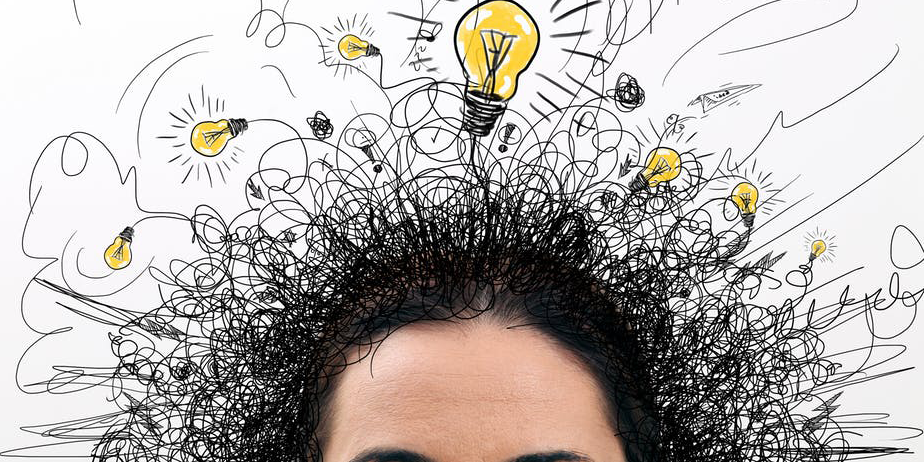 A person’s forehead and dark hair are visible at the bottom, with chaotic black scribbles and several yellow light bulbs sketched above their head, symbolizing creative ideas and mental activity.