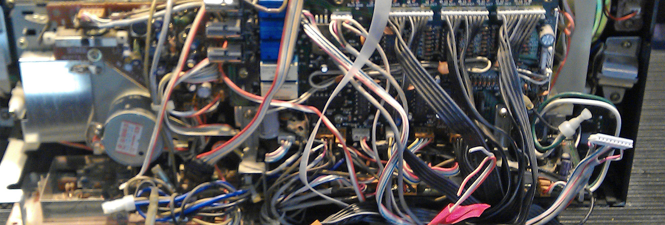 Close-up of the inside of an electronic device showing a complex arrangement of circuit boards, components, and many tangled, multicolored wires.