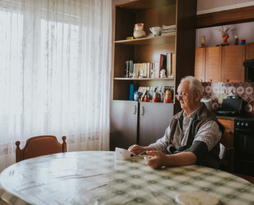 Senior man taking his blood pressure at home on the kitchen table.