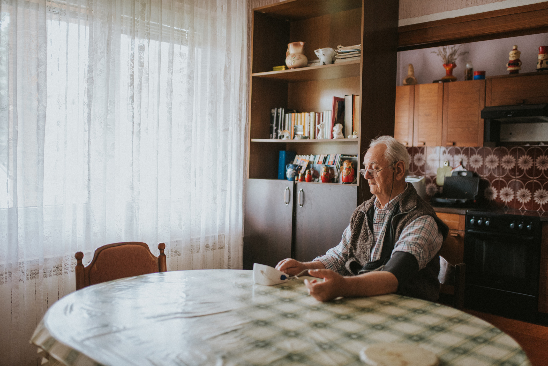 Senior man taking his blood pressure at home on the kitchen table.